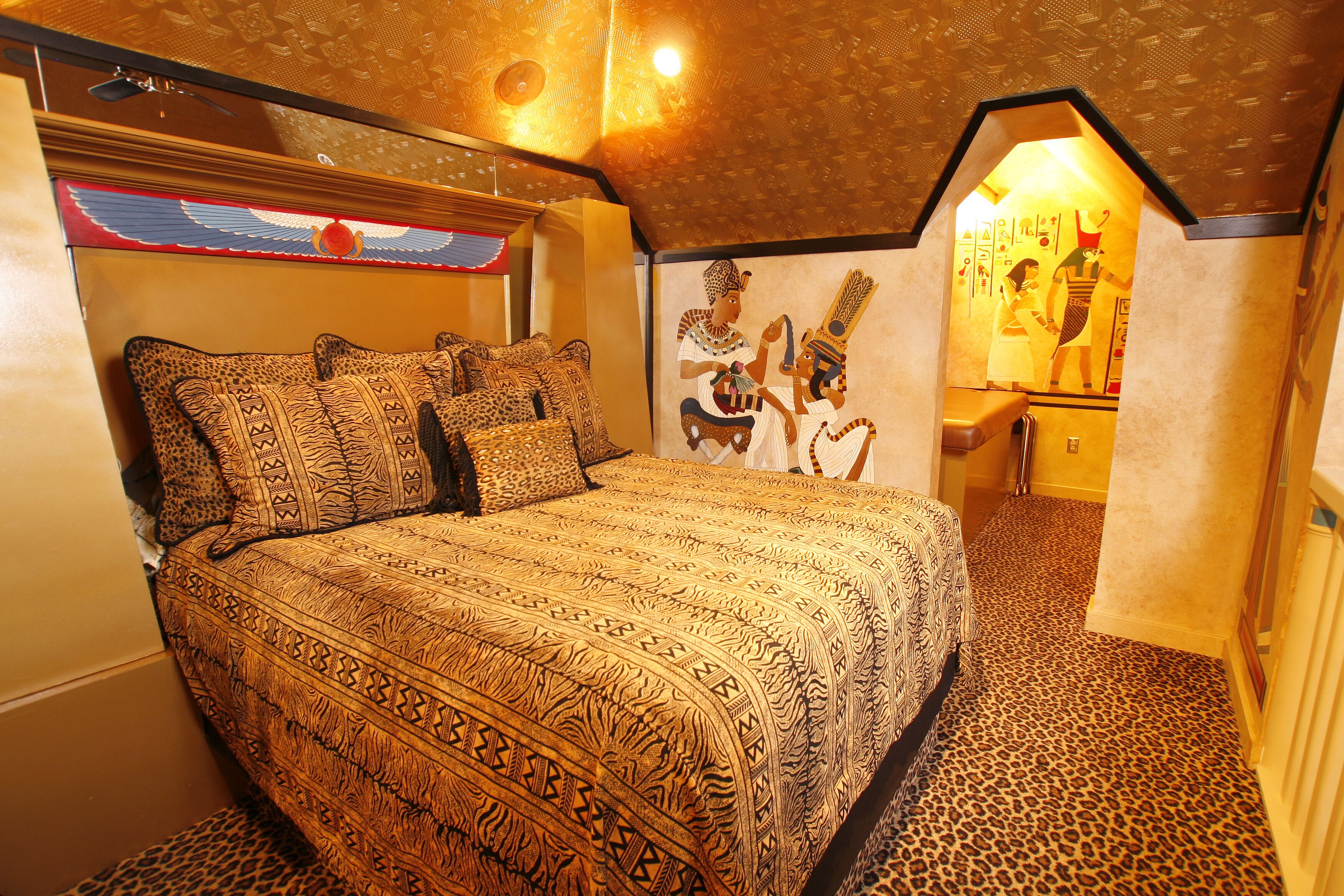 Une chambre à coucher avec un lit recouvert d’une couvre-lit à motifs, une fresque murale et un tapis à imprimé léopard.