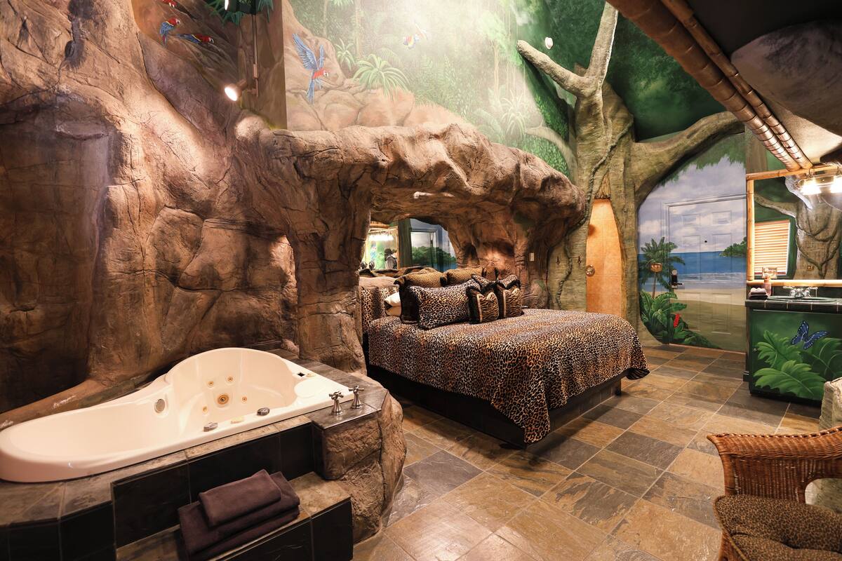 A room with a large bathtub, a bed with a leopard print bedspread, and a mural of a tree and jungle.