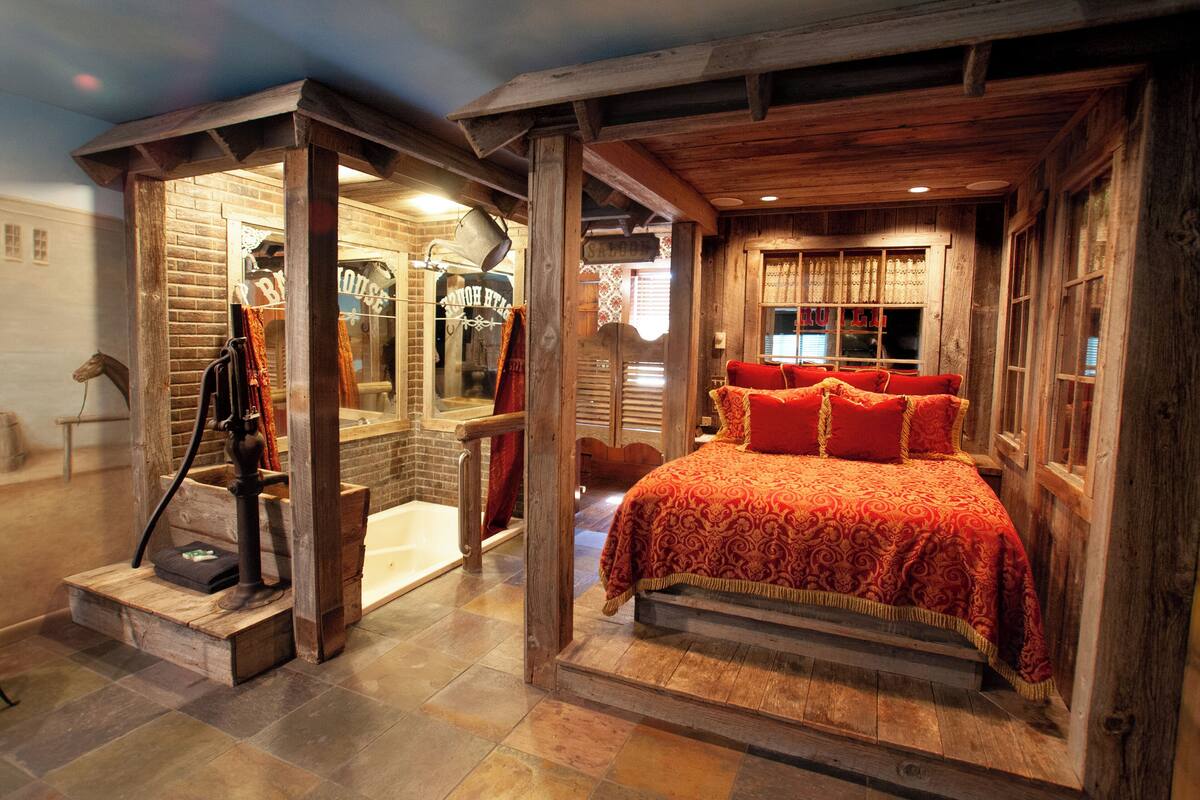 A rustic bedroom with a wooden bed, a small bathroom with a bathtub, and a visible window.