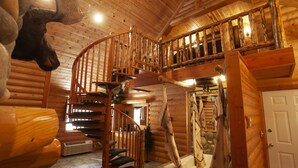 A log cabin interior with a spiral staircase, a mounted moose head, and a stone fireplace. - Black Swan Inn (Pocatello)