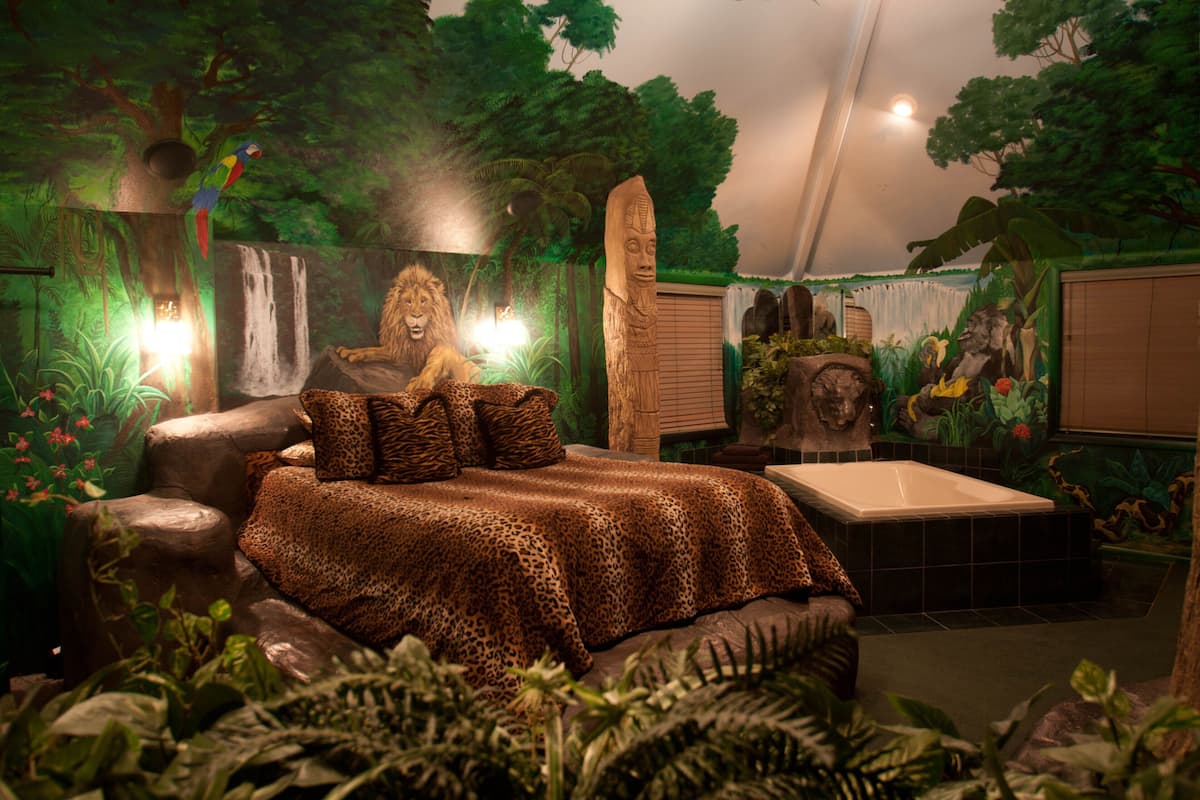 A room with a bed, a bathtub, and a mural of a jungle scene.