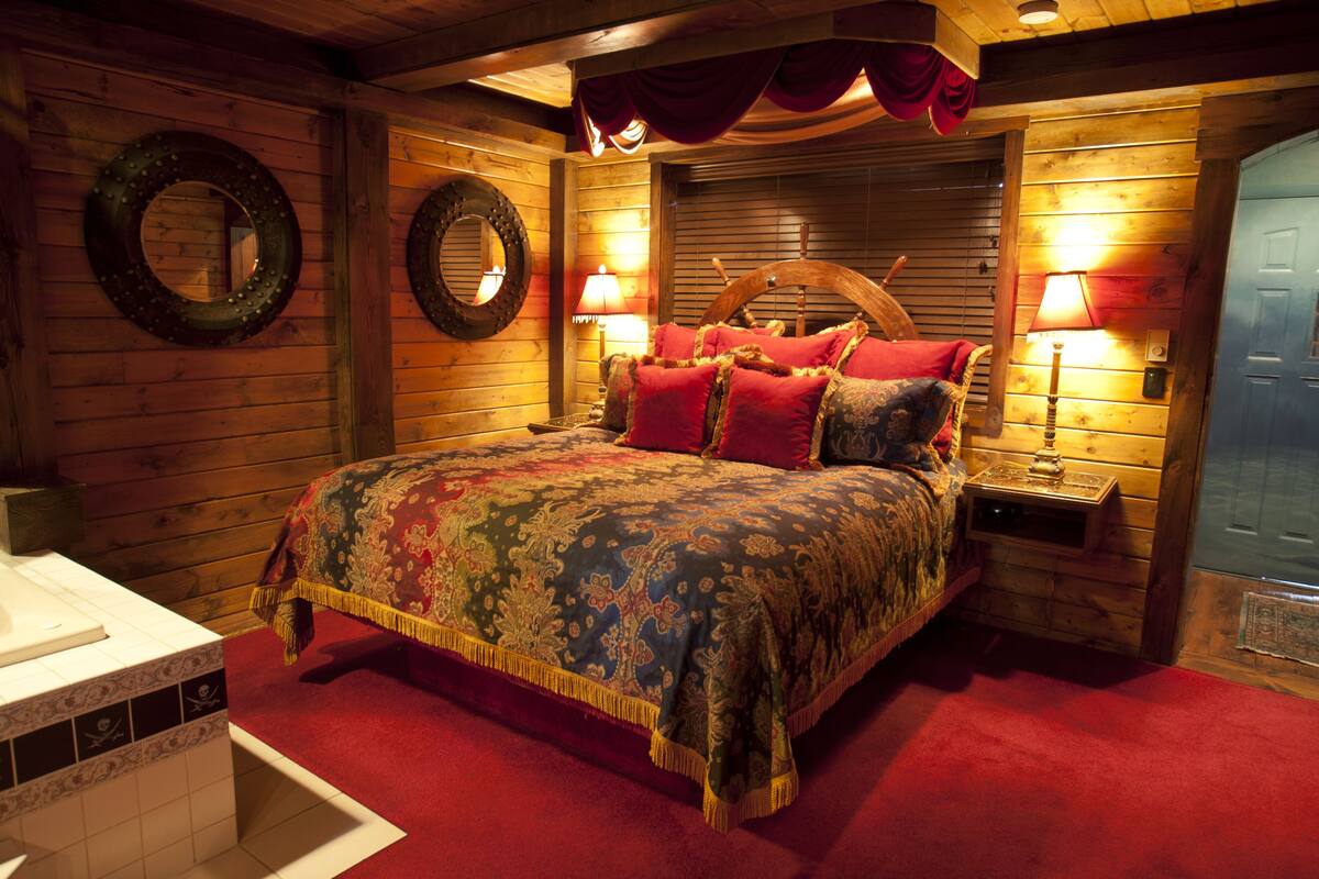 A wooden cabin-style bedroom with a large bed, two bedside lamps, and a wooden headboard.