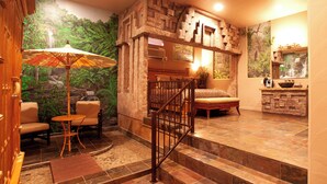 A room with a stone wall, a wooden staircase, a sofa, and a small table with an umbrella. - Destinations Inn (Idaho Falls)