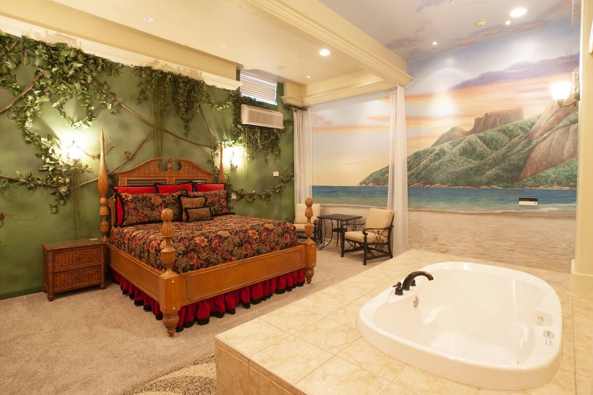 A bedroom with a large bed, a bathtub, and a mural of a beach scene.