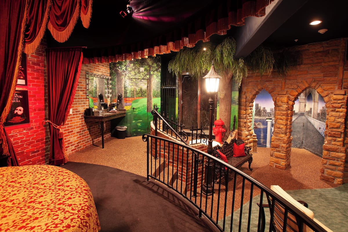 A room with a brick wall, a staircase, a bed, and a red fire hydrant.