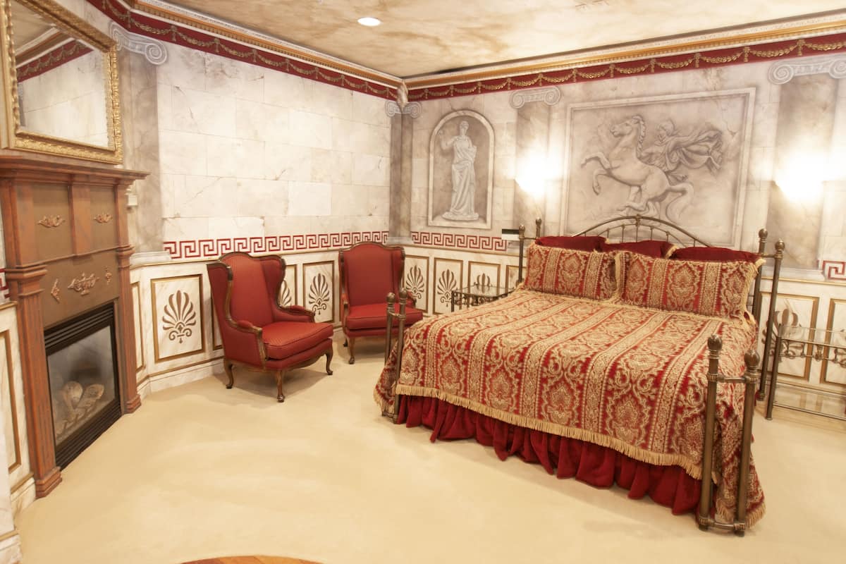 A room with a large bed, a fireplace, and a red armchair.