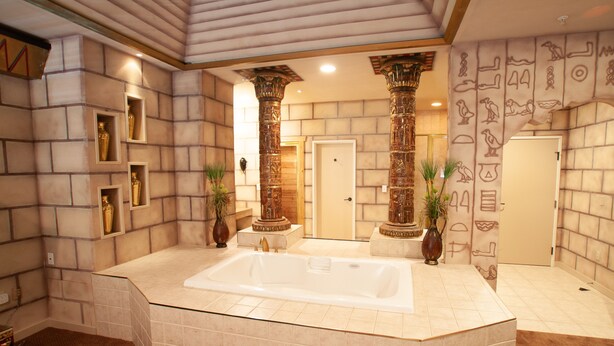 A spacious bathroom with a large bathtub, two ornate columns, and decorative wall art. - Destinations Inn (Idaho Falls)
