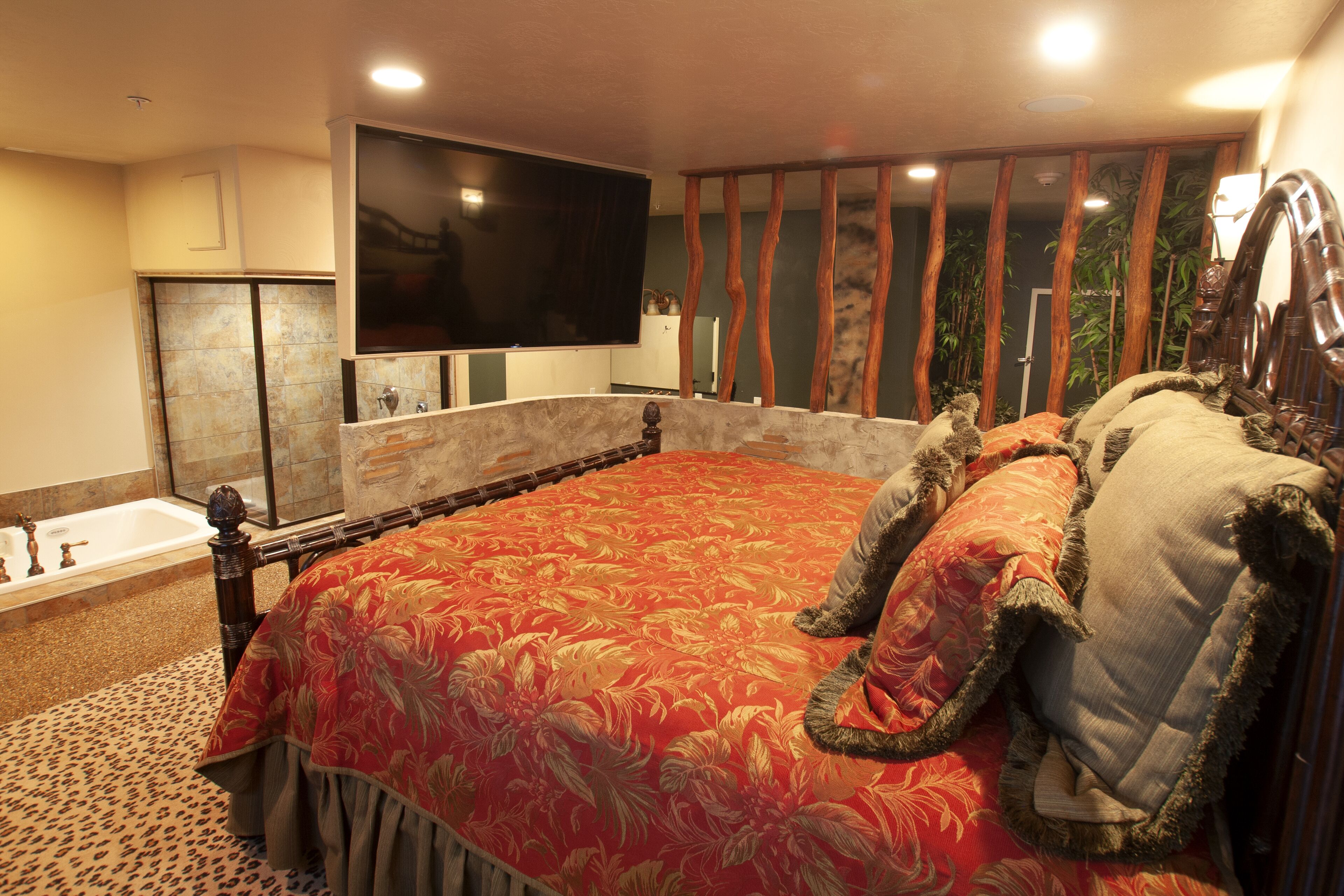 Une chambre à coucher avec un grand lit, un téléviseur à écran plat fixé au-dessus, une baignoire et une tête de lit en bois.