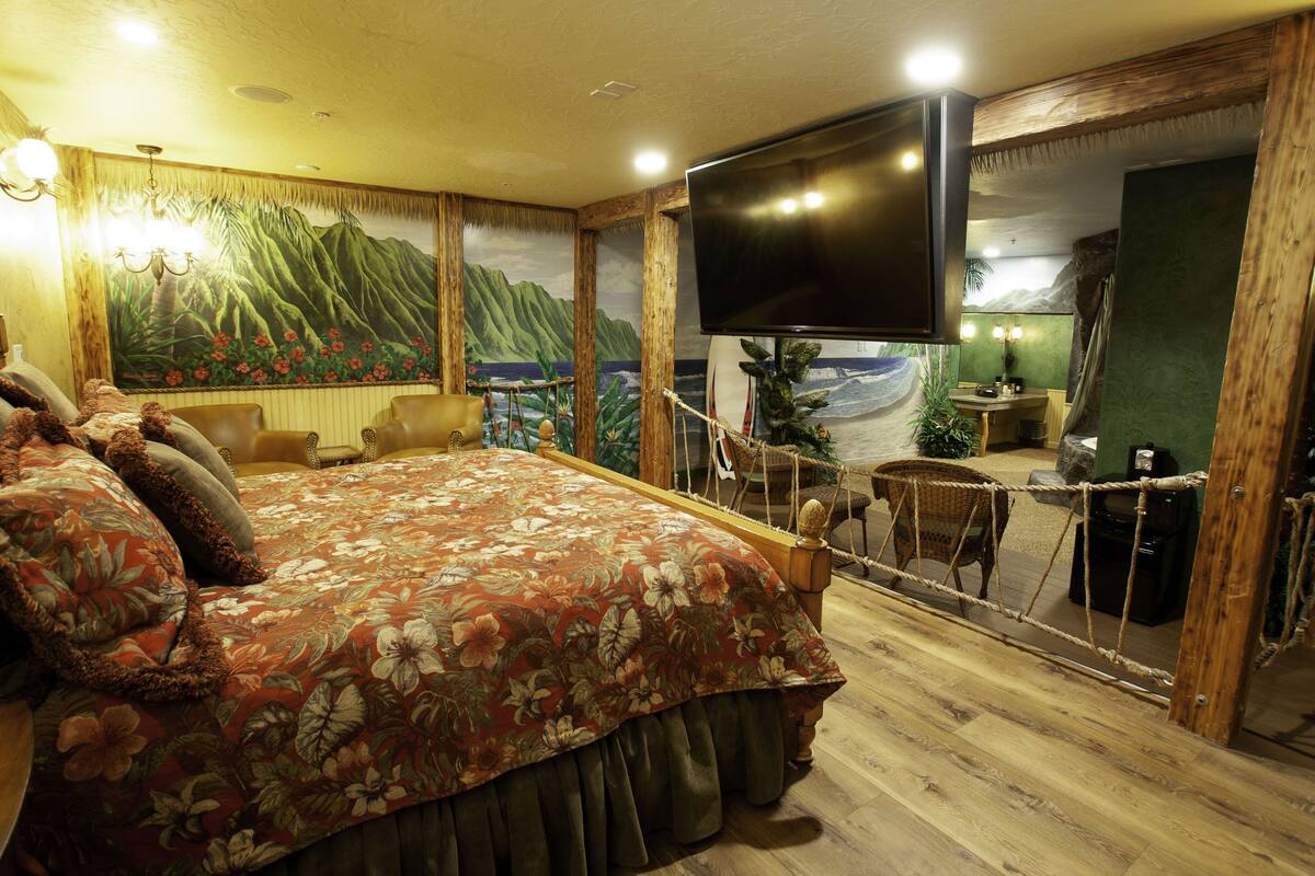 A bedroom with a large bed, a TV, a wooden floor, and a view of the ocean through a glass door.
