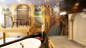 A luxurious bathroom with a large bathtub, a wooden bench, and a view of a canal with buildings. - Destinations Inn (Idaho Falls)