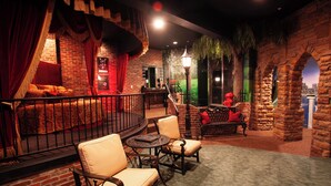 A cozy indoor setting with a brick wall, a red curtain, a bed, and a seating area with chairs and a table. - Destinations Inn (Idaho Falls)