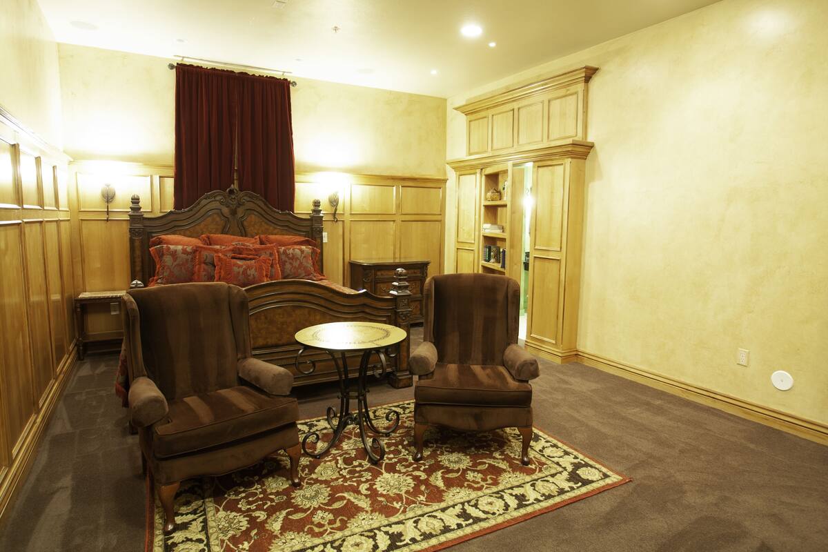A room with a bed, two armchairs, a small table, and a cabinet.