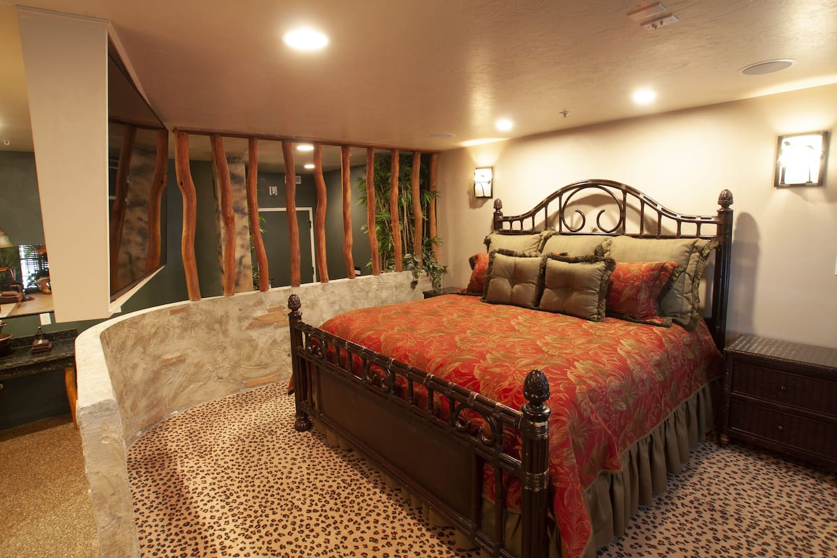 A bedroom with a bed, a wooden headboard, a stone bench, and a patterned carpet.