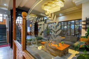 Um interior moderno com escada de madeira, um lustre grande e uma área de estar com mesa de centro e plantas.