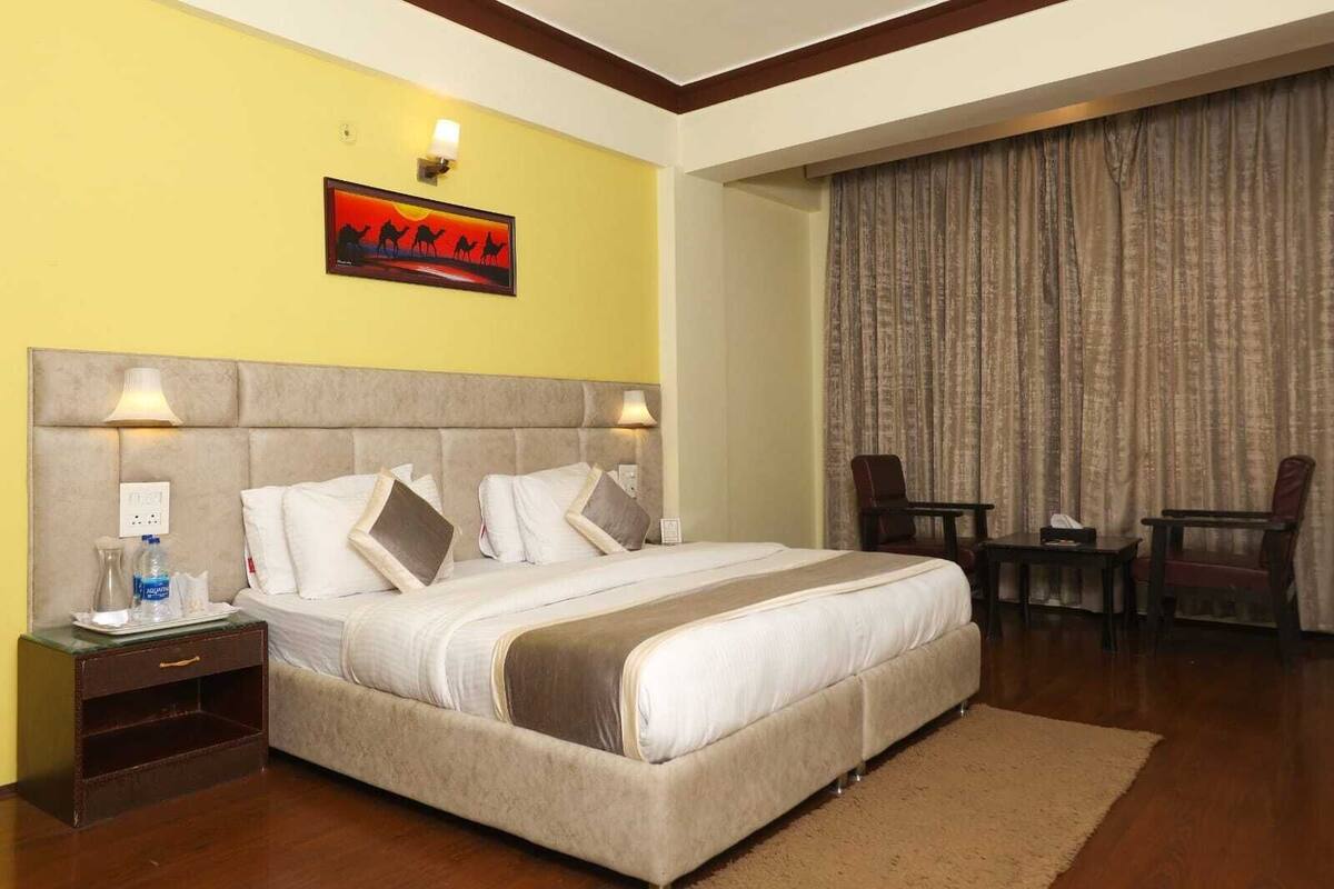 A hotel room with a large bed, two bedside lamps, a nightstand with a water bottle, a chair, and a table.