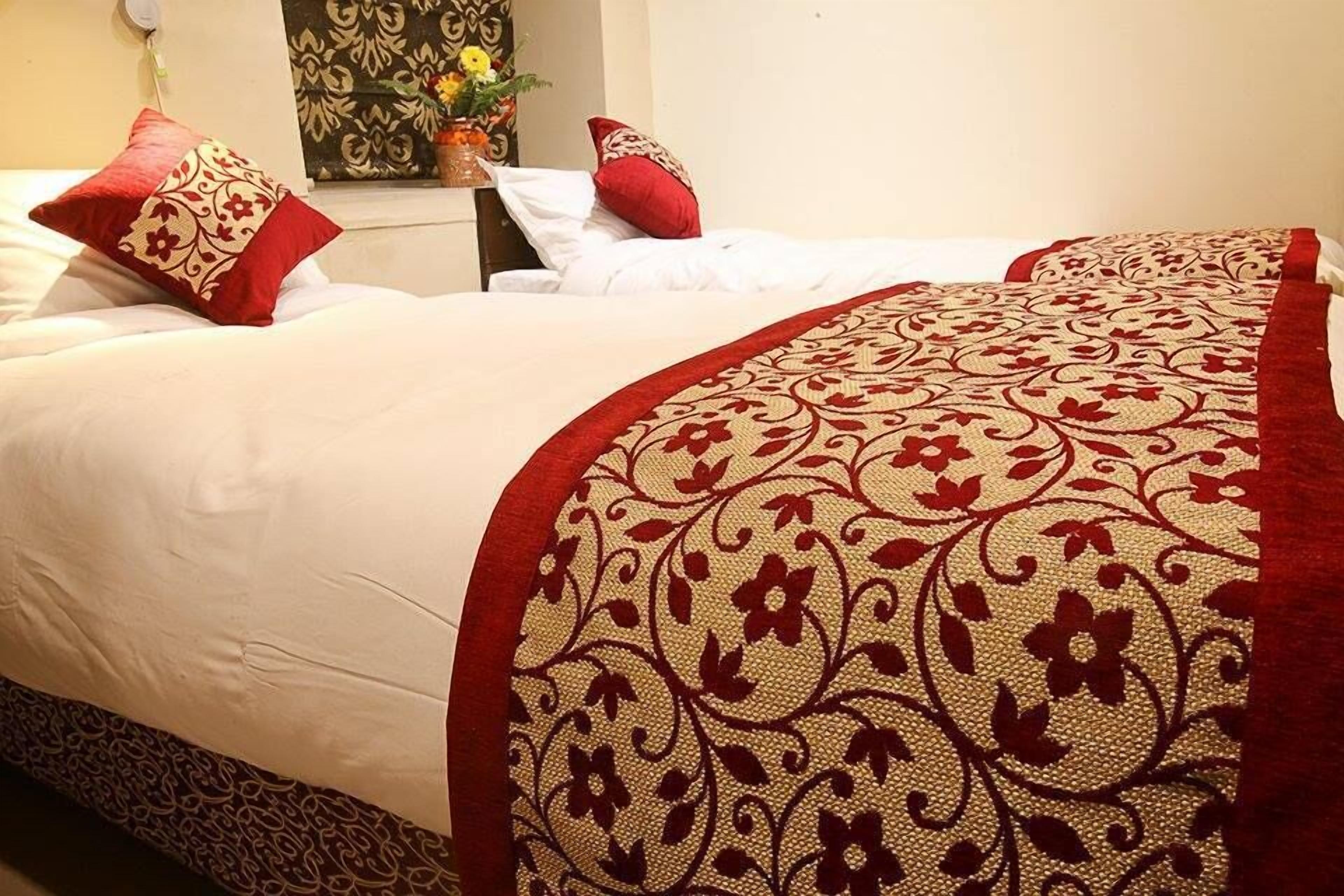 A neatly made bed with a red and beige patterned bedspread and matching pillows.