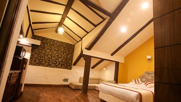 Una habitación con techo inclinado, una cama, un sofá y una mesita.