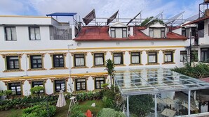 Un hotel con un invernadero de vidrio, múltiples ventanas con marcos decorativos y una azotea con paneles solares.