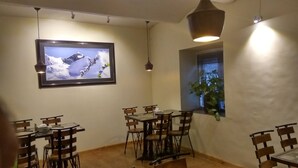 Un área de comedor con un cuadro grande en la pared, varias mesas y sillas, y una ventana con una planta.