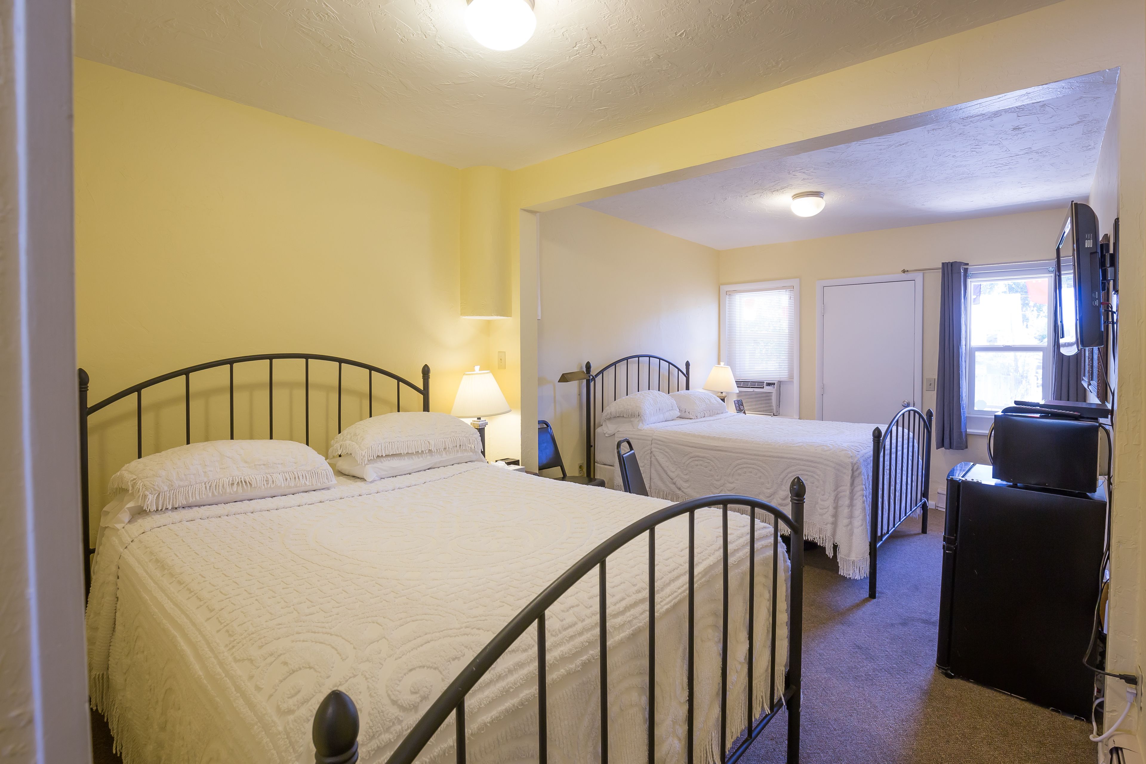 A hotel room with two single beds, a desk, a chair, a television, and a window with curtains.