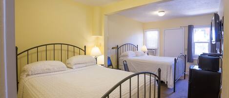 A hotel room with two single beds, a desk, a chair, a television, and a window with curtains.