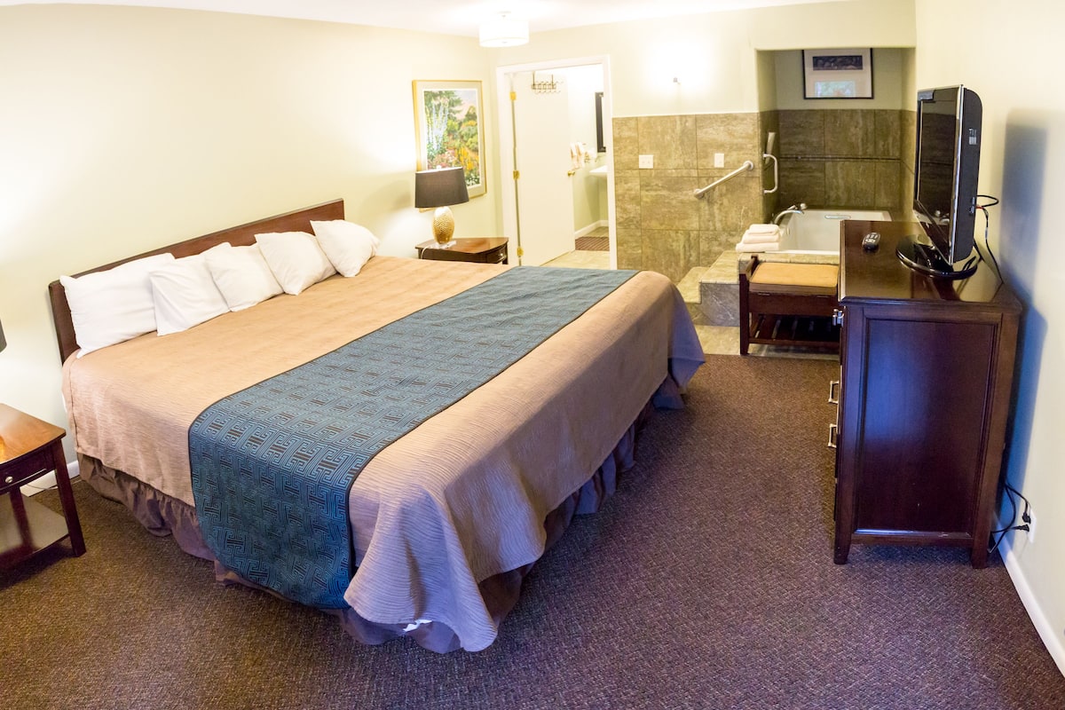 A hotel room with a large bed, a bathroom with a bathtub, a desk, and a television.