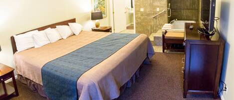 A hotel room with a large bed, a bathroom with a bathtub, a desk, and a television.