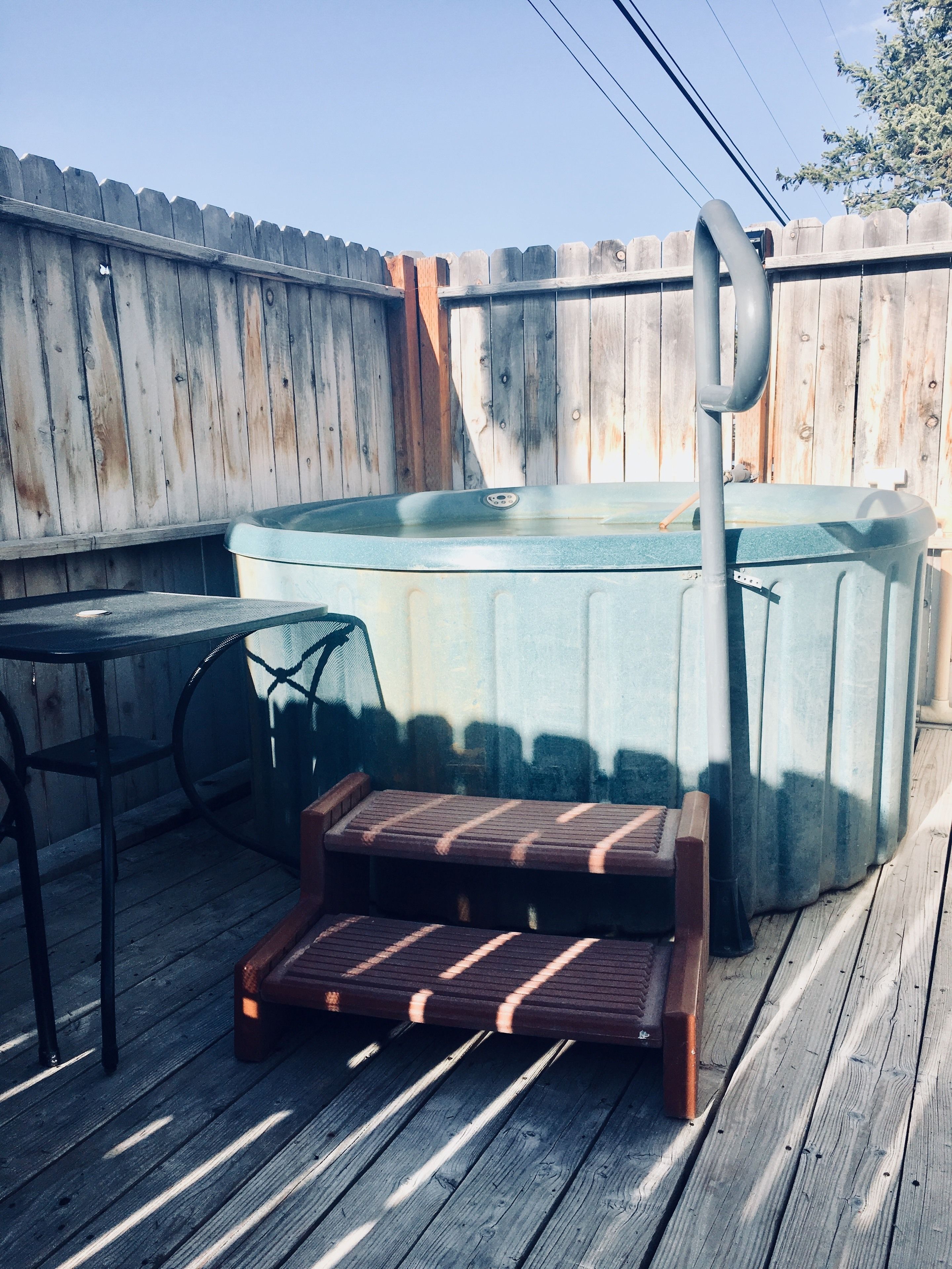 A hot tub with steps leading up to it, a metal table, and a wooden deck.