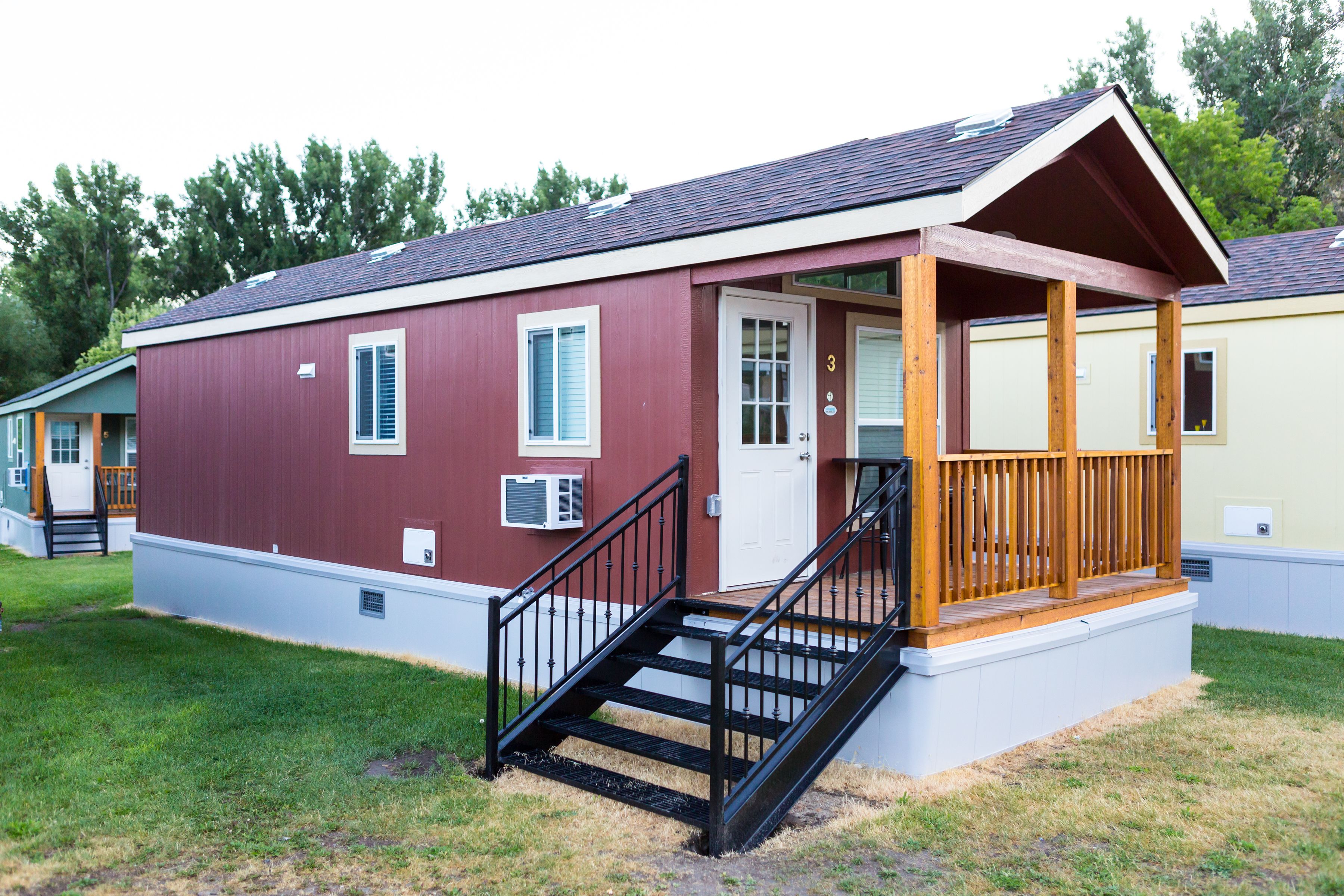 A single-story building with a red exterior, white trim, and a wooden porch. There are steps leading up to the porch, and a door with a window above it.