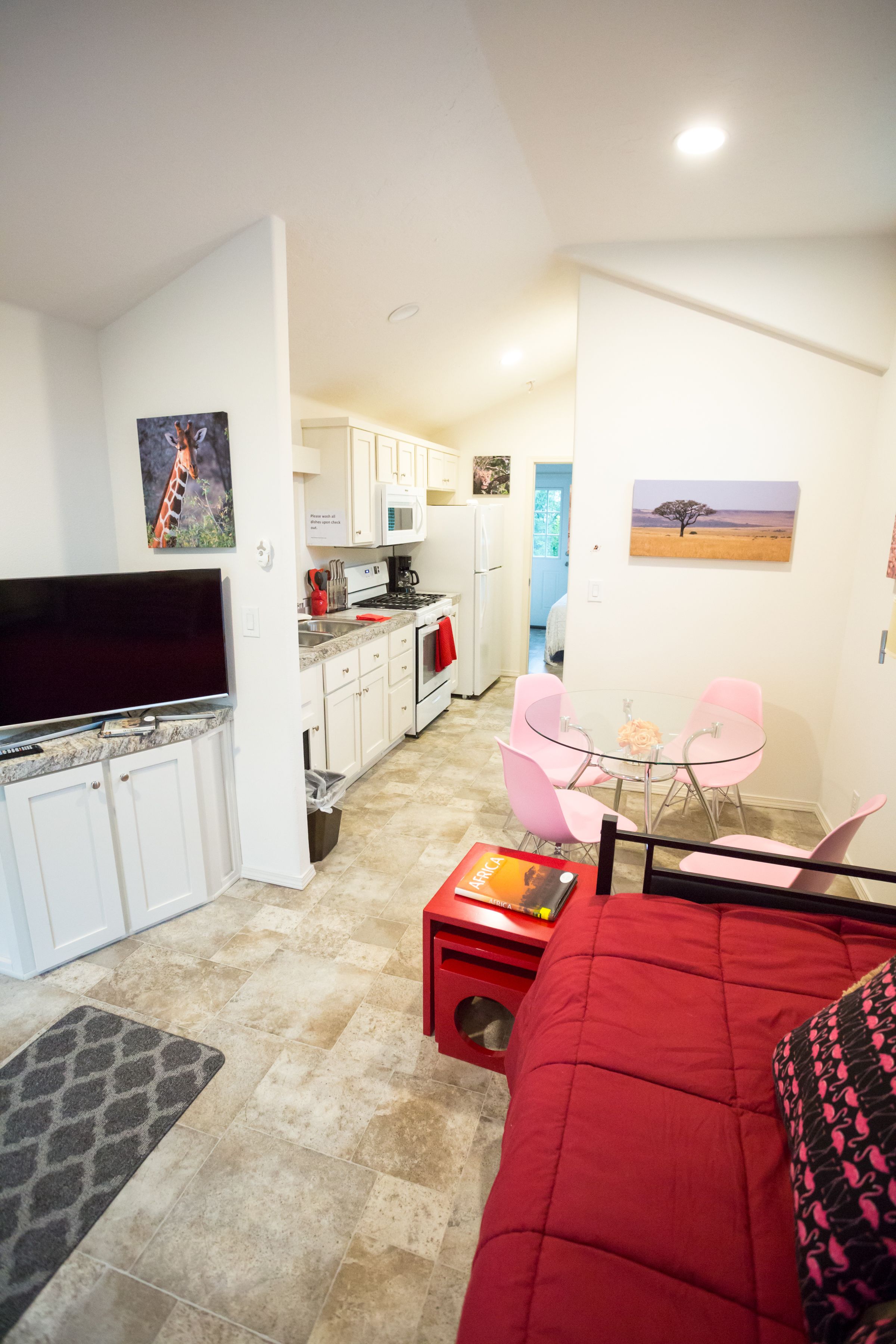A compact living space with a kitchenette, a dining area with pink chairs, a red sofa, and artwork on the walls.