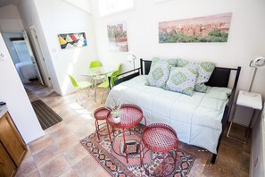 Ein Schlafzimmer mit einem Bett, zwei roten Metalltischen, einem grünen Stuhl und einem gemusterten Teppich.