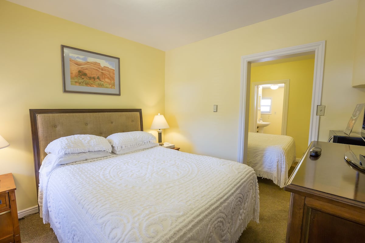 A hotel room with a large bed, a bedside table, a lamp, a nightstand, and a framed picture on the wall.