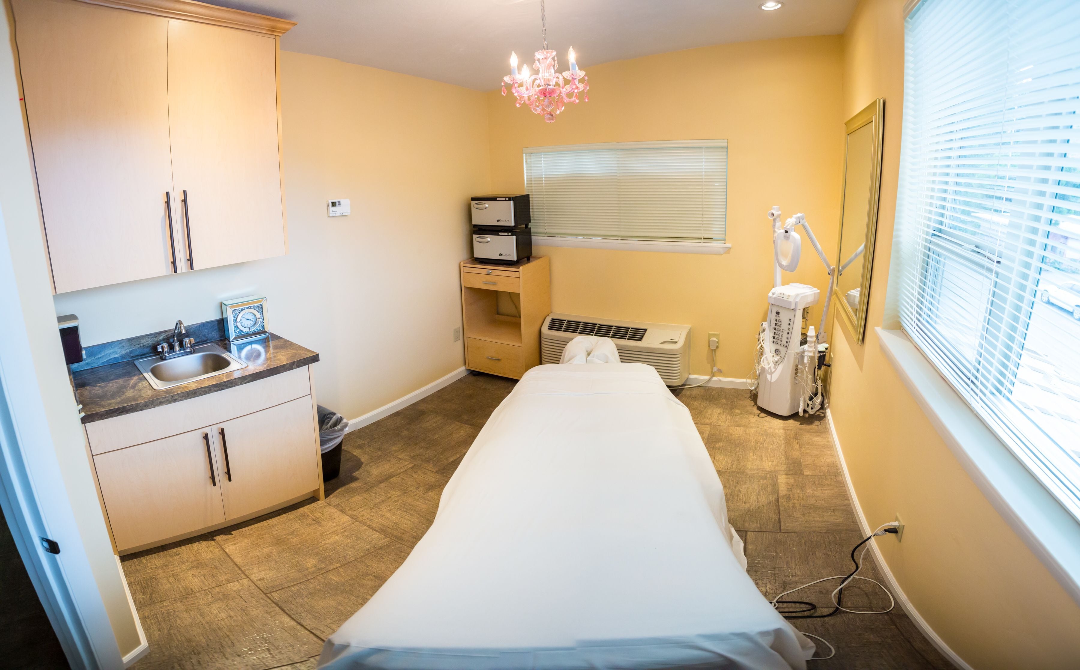 Une petite pièce bien éclairée, équipée d’un lit, d  ’un bureau, d’une chaise, d’un lavabo et d’une fenêtre avec des stores.