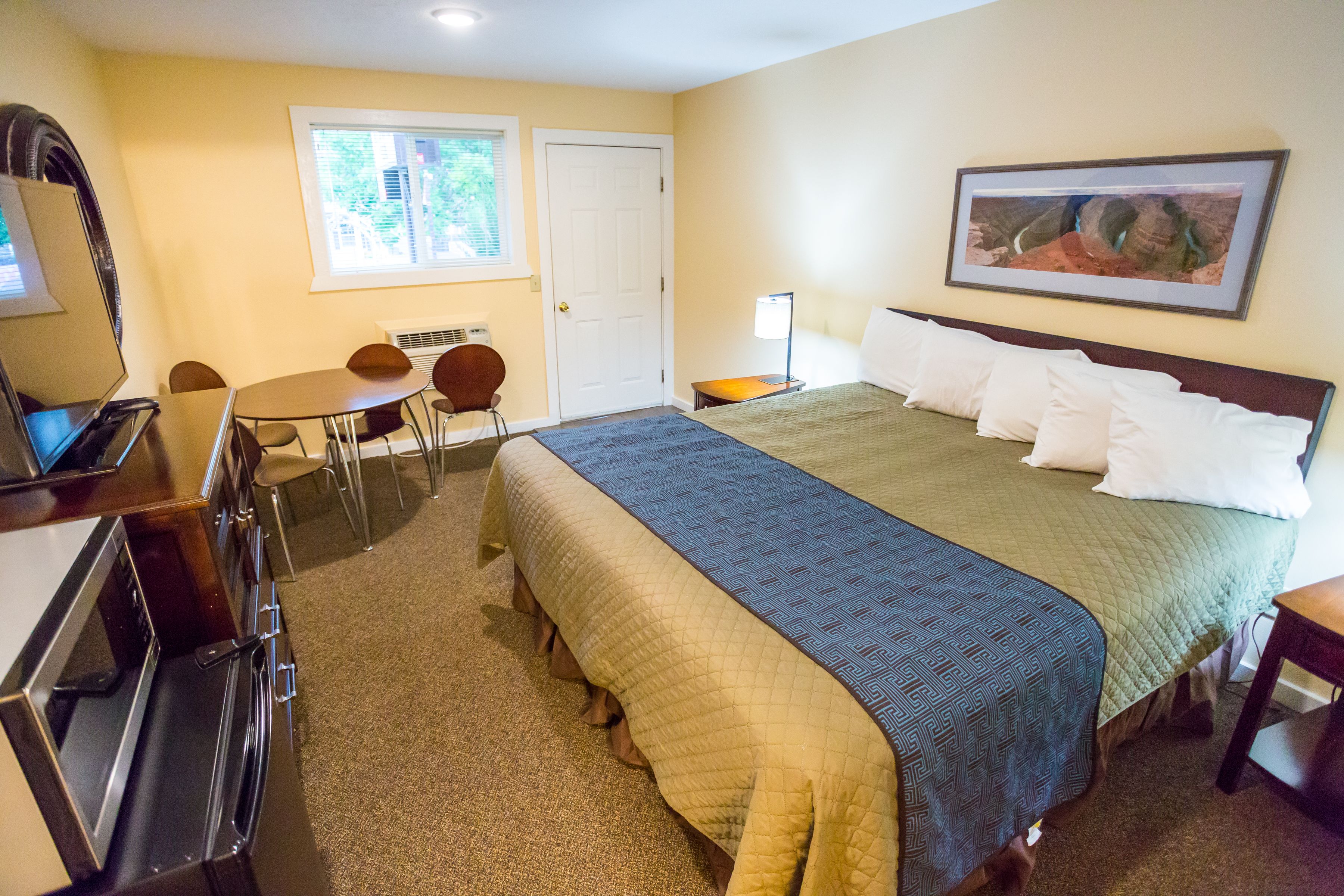 Une chambre d’hôtel avec un lit, un bureau, une chaise, une lampe et un tableau au mur.