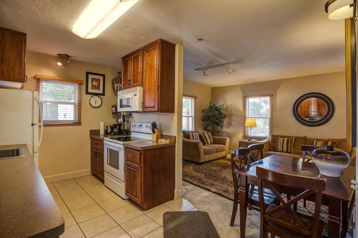 A kitchen with wooden cabinets, a stove, and a microwave. There is a dining area with a table and chairs.