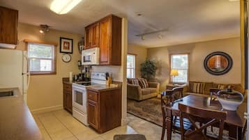 Una cocina con armarios de madera, una estufa y un microondas. Hay una zona de comedor con una mesa y sillas.