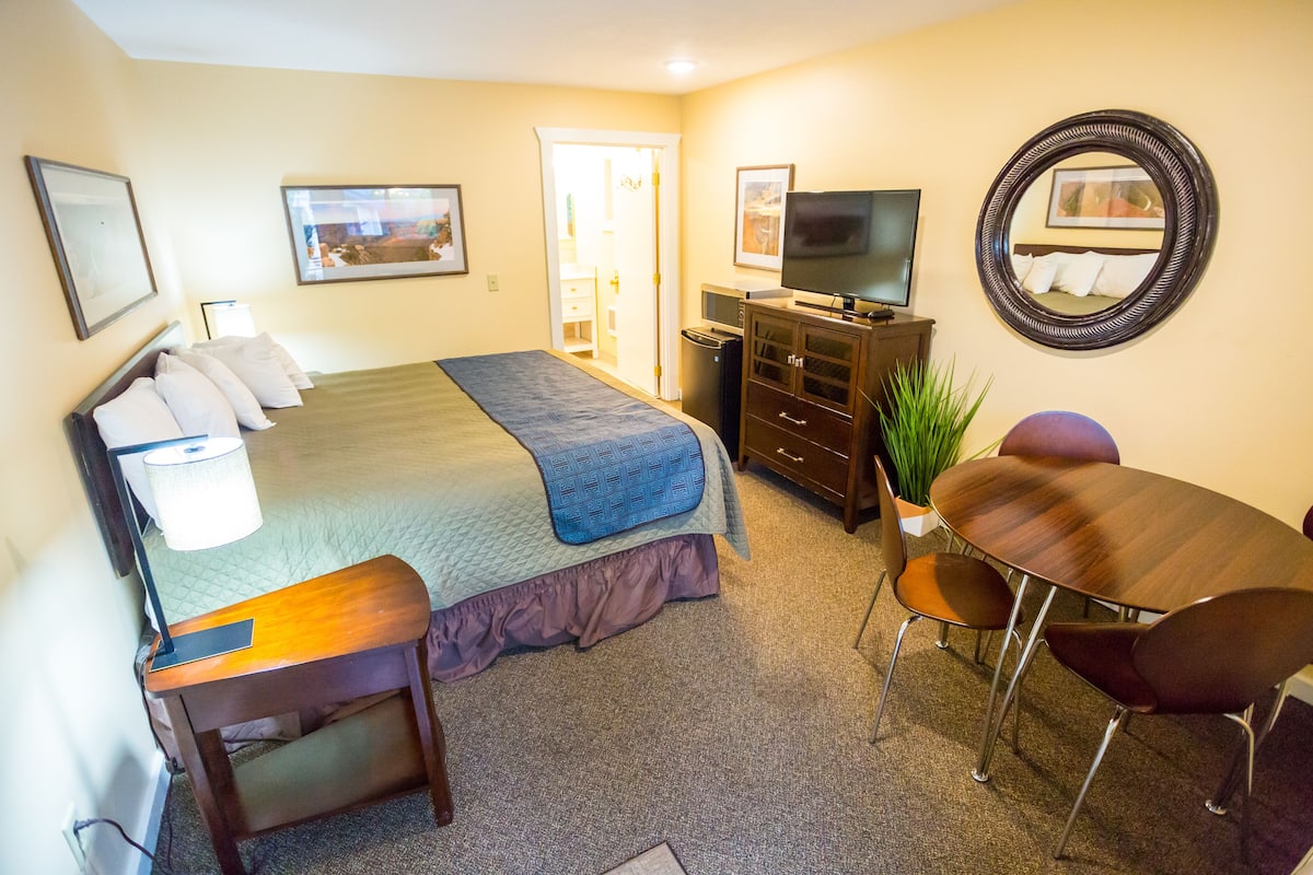 A hotel room with a bed, a TV, a desk, and a dining table.