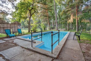 A rectangular swimming pool with a metal safety railing, surrounded by a concrete deck and a wooden fence.