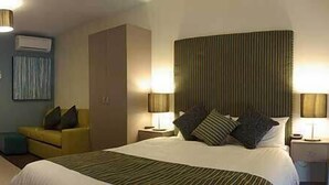 Habitación de hotel con cama, lámparas de noche, una silla, escritorio y equipo de aire acondicionado.