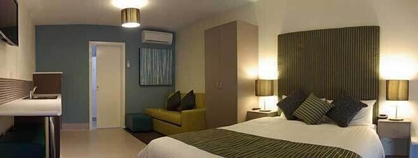 A hotel room with a bed, bedside lamps, a chair, a desk, and an air conditioning unit. - Shearwater Motel BIG4 Port Fairy (Port Fairy)