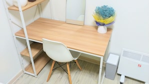 A compact workspace with a wooden desk, white chair, and a small shelf with potted plants.