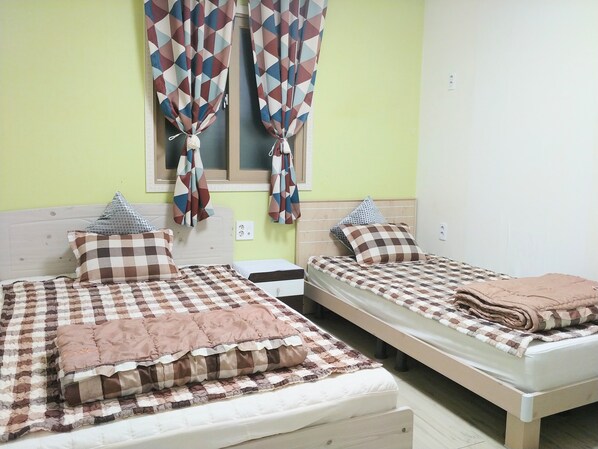 Two single beds with checkered bedding, a window with curtains, and a bedside table.