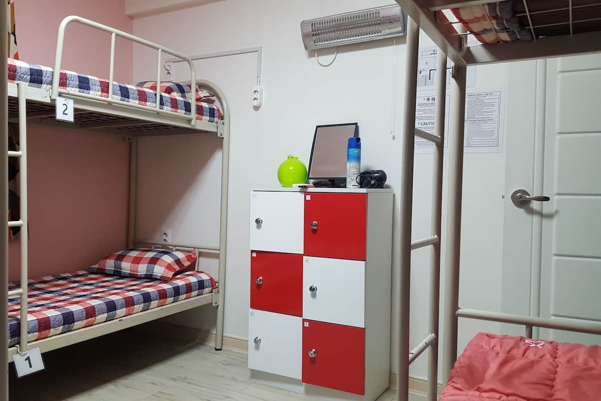 Habitación con literas, un armario rojo y blanco, un calentador y una puerta con un cartel.