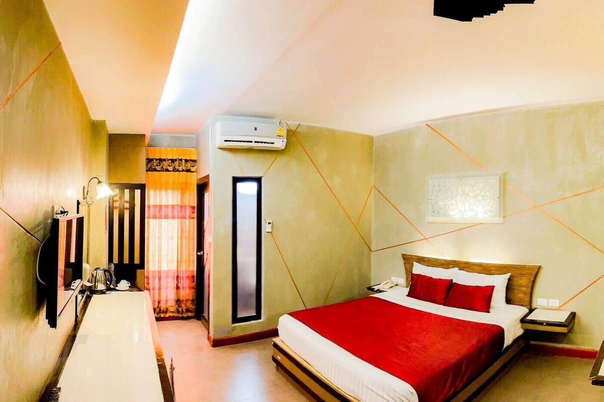 Una habitación de hotel con cama, mesita de noche y espejo. Hay una puerta que da a otra habitación.