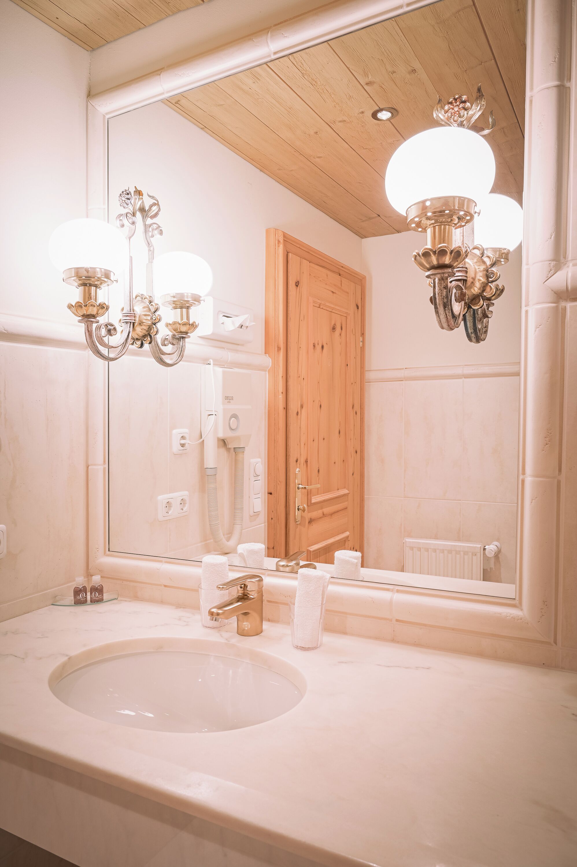 Une salle de bain avec un grand miroir, un lavabo, un lustre et une porte en bois.
