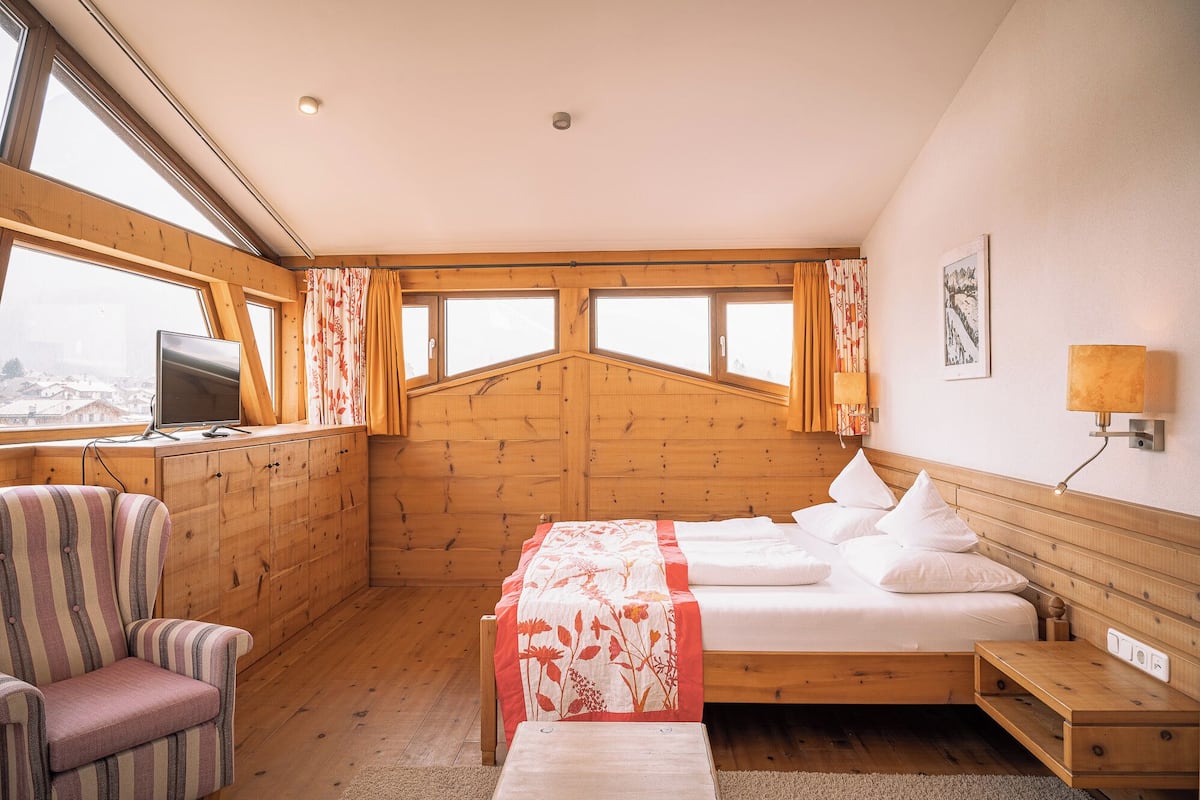Ein gemütliches Zimmer mit einem Bett, einem Sessel, einem Schreibtisch und einem Fenster mit Blick auf eine verschneite Landschaft.