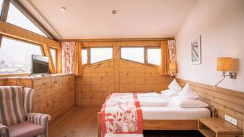 A cozy room with a bed, a chair, a desk, and a window overlooking a snowy landscape.