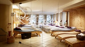 Sala de spa com várias mesas de massagem, bancos de madeira e uma divisória de vidro.