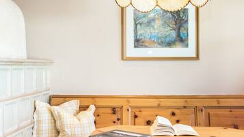 Una habitación con un banco de madera, una mesa con un libro abierto, un cuadro enmarcado en la pared y un armario blanco.