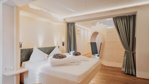 Quarto de hotel moderno com cama de madeira, mesa de cabeceira e vista através de uma porta aberta.